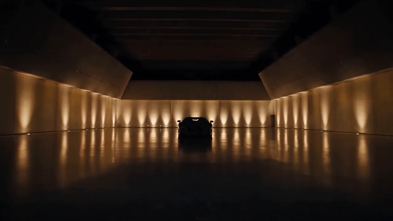 Opening frame of the Revuelto film: a dark, amber-lit hall with a supercar waiting at the far end and its reflection on the polished floor